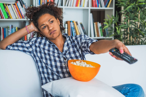 Tylsistynyt nainen istuu kotona kaukosäädin television katseluun
 - Valokuva, kuva