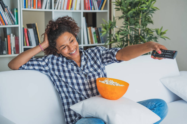 Afrofrau sitzt zu Hause mit Fernbedienung vor dem Fernseher - Foto, Bild