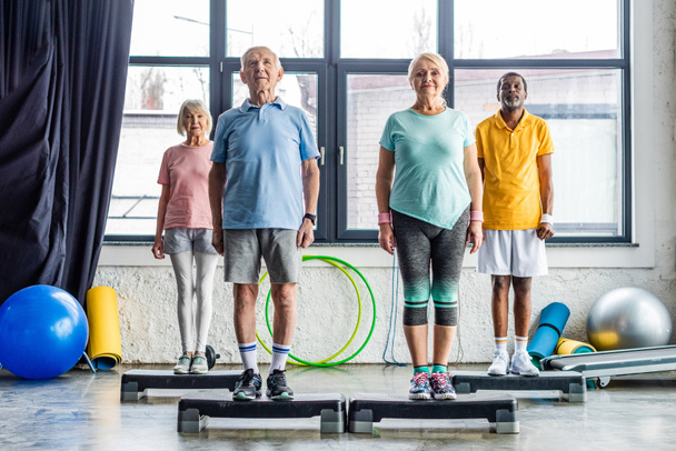 atletas seniores multiétnicos exercício síncrono em plataformas de degrau no ginásio
 - Foto, Imagem
