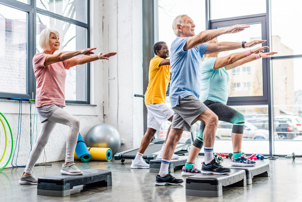 atletas seniores exercício síncrono em plataformas de degrau no ginásio
 - Foto, Imagem