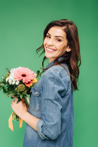 attractive woman holding flower bouquet and looking at camera isolated on green - Foto, afbeelding