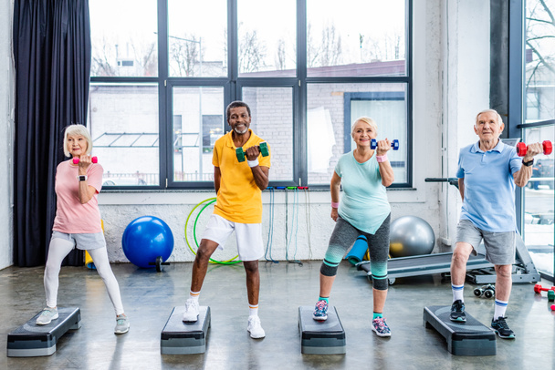 deportistas multiculturales senior feliz ejercicio sincrónico con pesas en plataformas de paso en el gimnasio
 - Foto, imagen