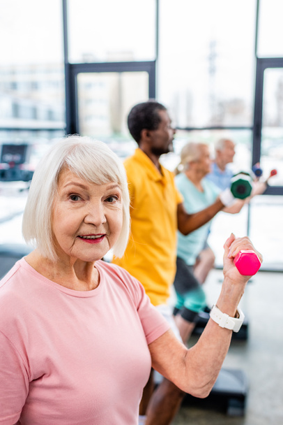 enfoque selectivo de la mujer mayor y sus amigos haciendo ejercicio con pesas en el gimnasio
 - Foto, Imagen