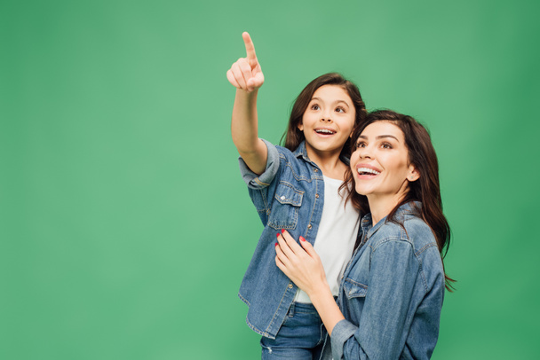 aufgeregte Tochter zeigt mit dem Finger, während glückliche Mutter isoliert auf Grün blickt - Foto, Bild