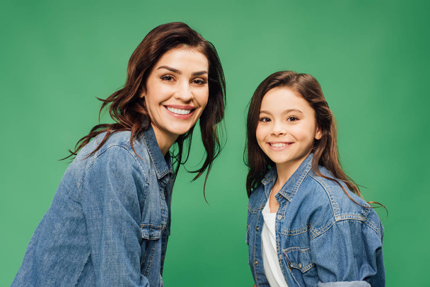 happy mother and daughter in denim looking at camera isolated on green - Foto, Imagen