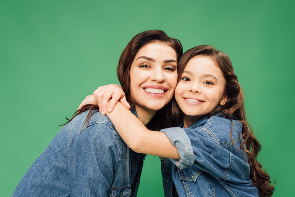 happy mother and daughter embracing and looking at camera isolated on green - Photo, Image