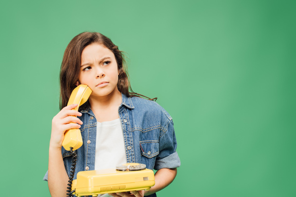 confused child in denim holding vintage telephone isolated on green - Foto, Imagen