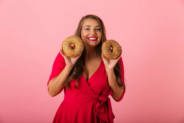 Image of a happy young woman isolated over pink wall background holding donuts. - Foto, imagen