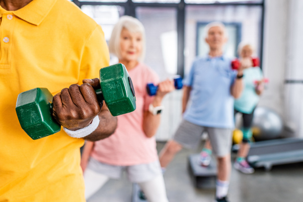 visão parcial de atletas seniores exercício síncrono com halteres no ginásio
 - Foto, Imagem