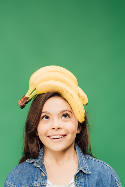 happy child holding bananas on head isolated on green  - Foto, Bild