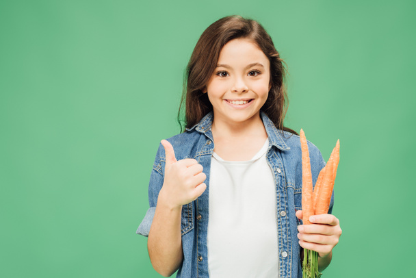 boldog gyermek gazdaság sárgarépa és bemutatás jel elszigetelt a zöld hüvelykujj - Fotó, kép
