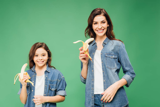 happy mother and daughter holding bananas isolated on green - Foto, immagini
