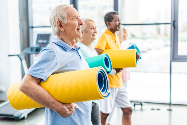 boční pohled na multethnic starší sportovci drží fitness rohože ve sportovní hale - Fotografie, Obrázek