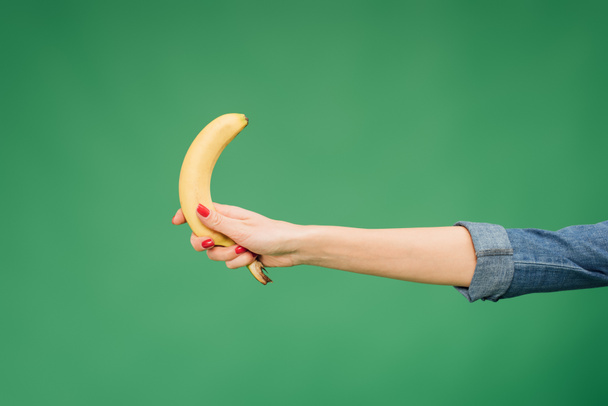 περικοπεί προβολή της γυναίκας κρατώντας μπανάνα στο χέρι απομονώνονται σε πράσινο - Φωτογραφία, εικόνα