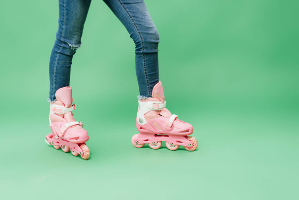 partial view of child wearing denim and pink rollerblades isolated on green - Photo, Image