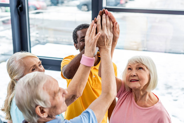 Blick aus der Vogelperspektive auf multikulturelle Senioren, die im Fitnessstudio die Hände zusammenlegen - Foto, Bild