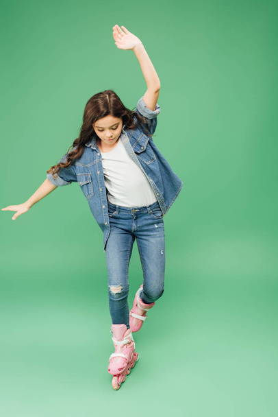 child in denim rollerblading with outstretched hands on green background - Fotoğraf, Görsel