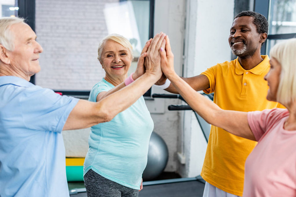 souriant athlètes seniors multiculturels empilant les mains ensemble à la salle de gym
 - Photo, image