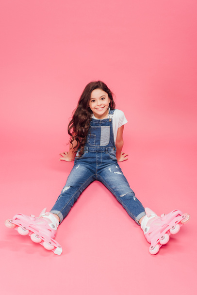 smiling child in overalls and roller blades looking at camera on pink background - Foto, Bild