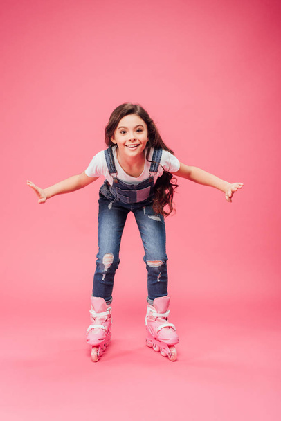 happy child in overalls rollerblading on pink background - Photo, Image