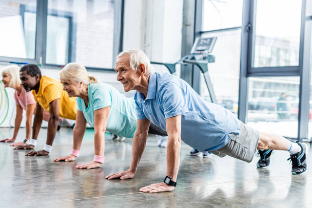Multikulti-Senioren synchron beim Planken im Fitnessstudio - Foto, Bild