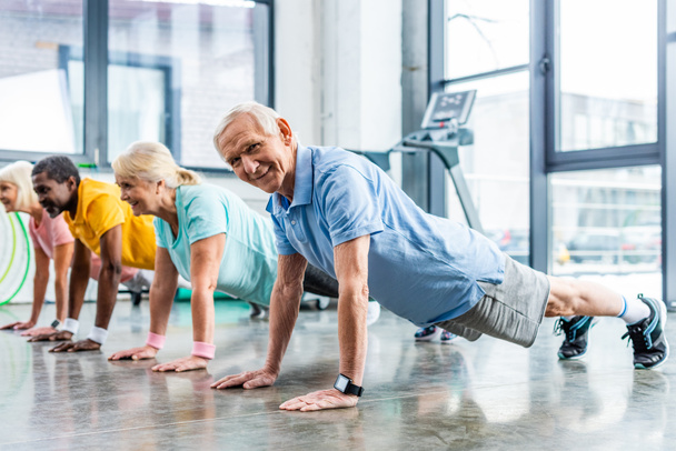 fröhliche multiethnische Senioren synchron beim Planken im Fitnessstudio - Foto, Bild