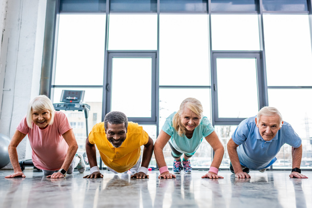 souriant multiethnique seniors sportifs synchrones faire planche à la salle de gym
 - Photo, image