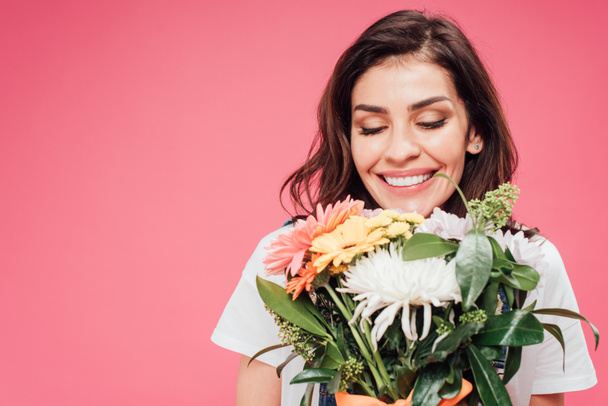beautiful woman with eyes closed holding flower bouquet isolated on pink - Foto, afbeelding