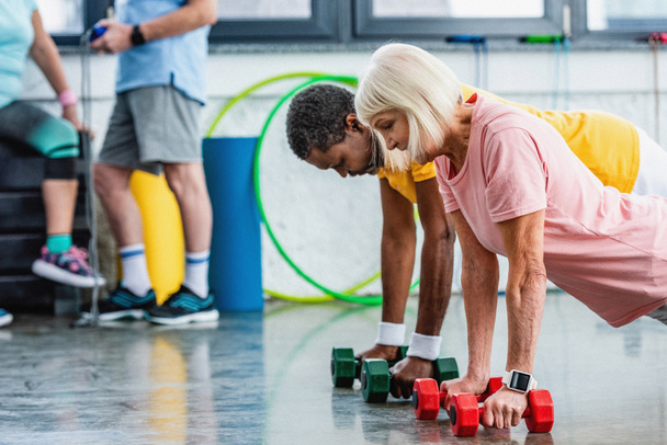 seçici odak ırklararası çift tahta spor salonunda dumbbells ile yapıyor - Fotoğraf, Görsel