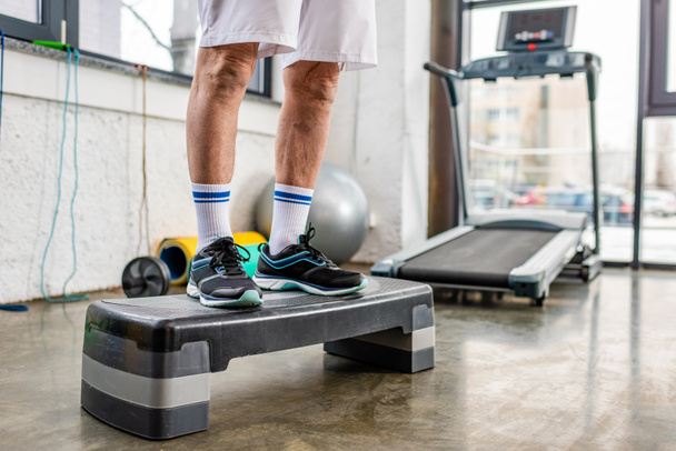 imagen recortada de atleta masculino senior de pie en la plataforma de paso en el gimnasio
 - Foto, Imagen