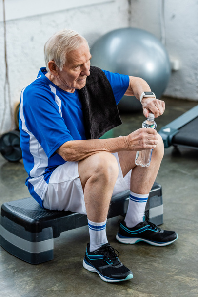 wysoki kąt widzenia sportowca starszy ręcznikiem, otwierając butelkę wody, odpoczynek w siłowni - Zdjęcie, obraz