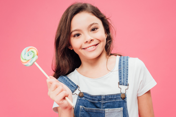 glimlachend kind bedrijf lollipop geïsoleerd op roze  - Foto, afbeelding