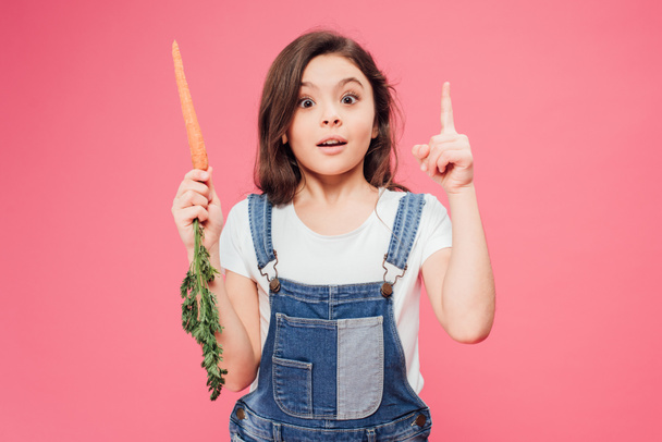 happy kid showing idea gesture and holding carrot isolated on pink  - 写真・画像