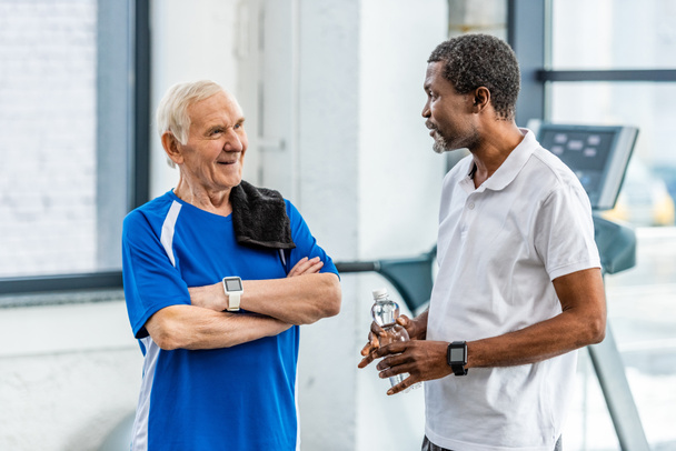 multicultural mature sportsmen talking to each other during rest at gym - Photo, Image