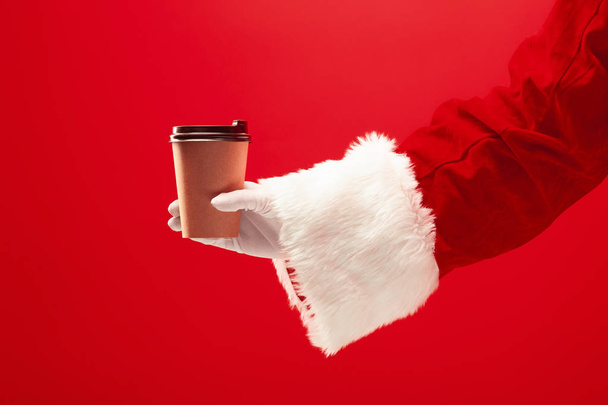 Christmas coffee. The Santa hand holding cup of cofee isolated on a red background with space for text - Valokuva, kuva