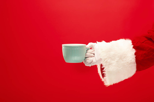 Christmas coffee. The Santa hand holding cup of cofee isolated on a red background with space for text - Fotó, kép