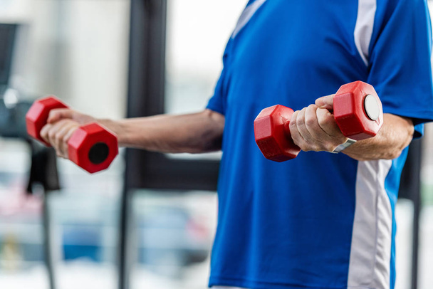 cropped image of senior sportsman exercising with dumbbells at gym - Foto, immagini