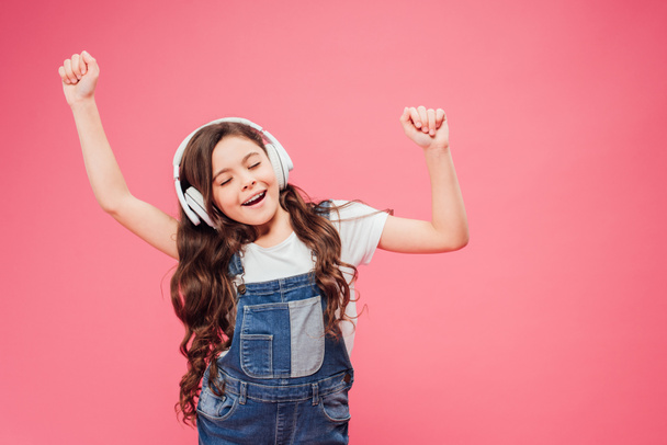 child with closed eyes and headphones dancing isolated on pink - Photo, Image