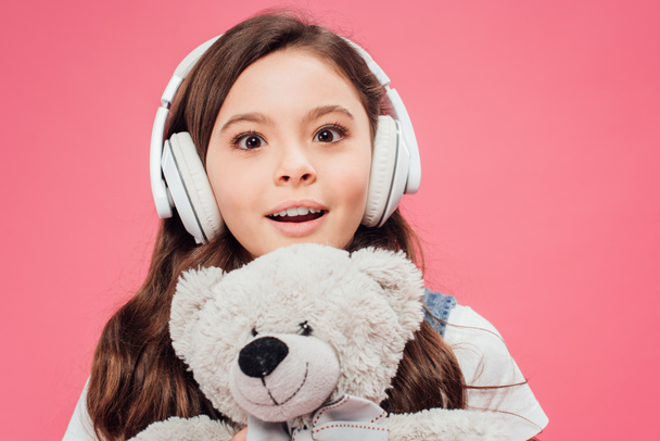 excited child in headphones holding teddy bear isolated on pink  - Zdjęcie, obraz