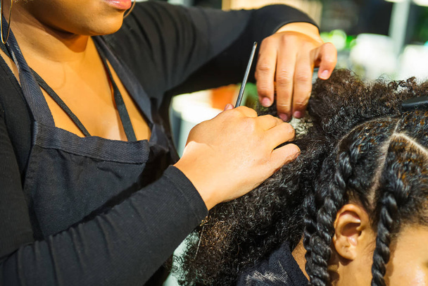 Close up african hairstylist braided hair of afro american female client in the barber salon. Black healthy hair culture and Style. Stylish therapy professional care concept. Selective focus - 写真・画像