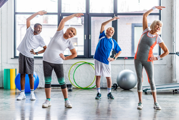 happy multiethnic senior sportspeople synchronous exercising at sports hall - Фото, изображение