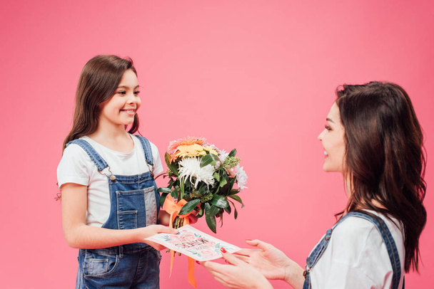 Veselá dcera dávat kartu a květy mamince na den matek izolované na růžové  - Fotografie, Obrázek