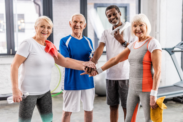 Счастливые старшие мультикультуральные друзья, взявшиеся за руки в спортзале
  - Фото, изображение