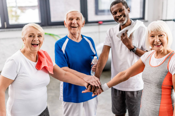 ridendo anziani sportivi multiculturali mettendo le mani insieme al palazzetto dello sport
  - Foto, immagini