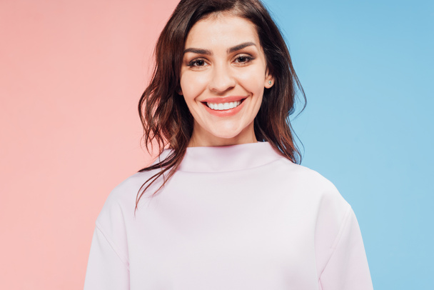 beautiful woman looking at camera and smiling on blue and pink background - Foto, immagini