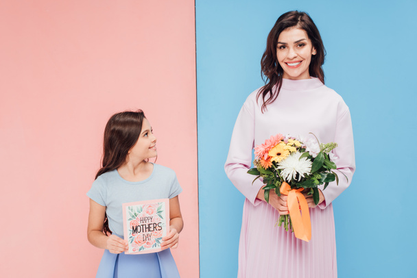 adorable child and attractive woman holding gifts on blue and pink background - Photo, Image