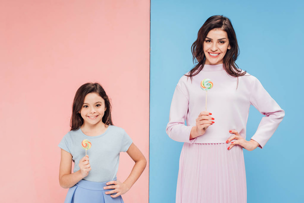 adorable child and attractive woman holding candies and looking at camera on blue and pink background - Photo, Image
