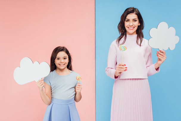 adorable child and attractive woman holding speech bubbles and candies on blue and pink background - Fotoğraf, Görsel