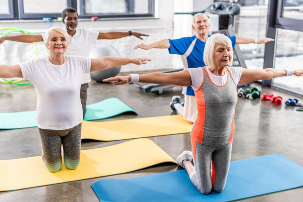 foco seletivo de atletas multiculturais seniores exercício síncrono em tapetes de fitness no ginásio
 - Foto, Imagem