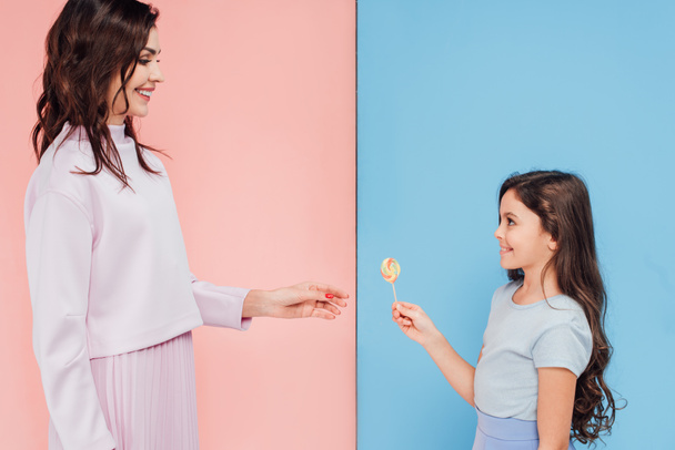 adorable child giving candy to woman on blue and pink background - Photo, Image